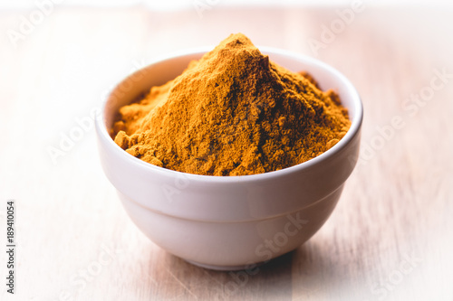 Indian spices: turmeric powder inside a white ceramic bowl on a wooden background.