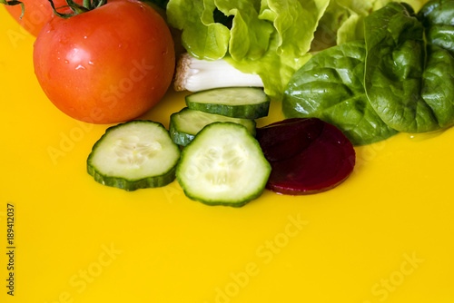 Fresh colourful salad ingredients, yellow background, room for text. Lettuce, spring onion, tomato, beetroot and cucumber slices, closeup.