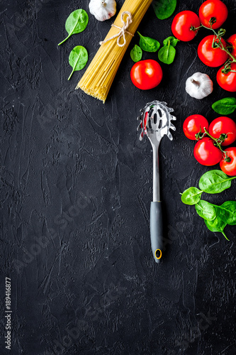 Italian pasta concept. Spaghetti, tomatoes, garlic, cheese grater, spoon for spaghetti on black background top view copy space