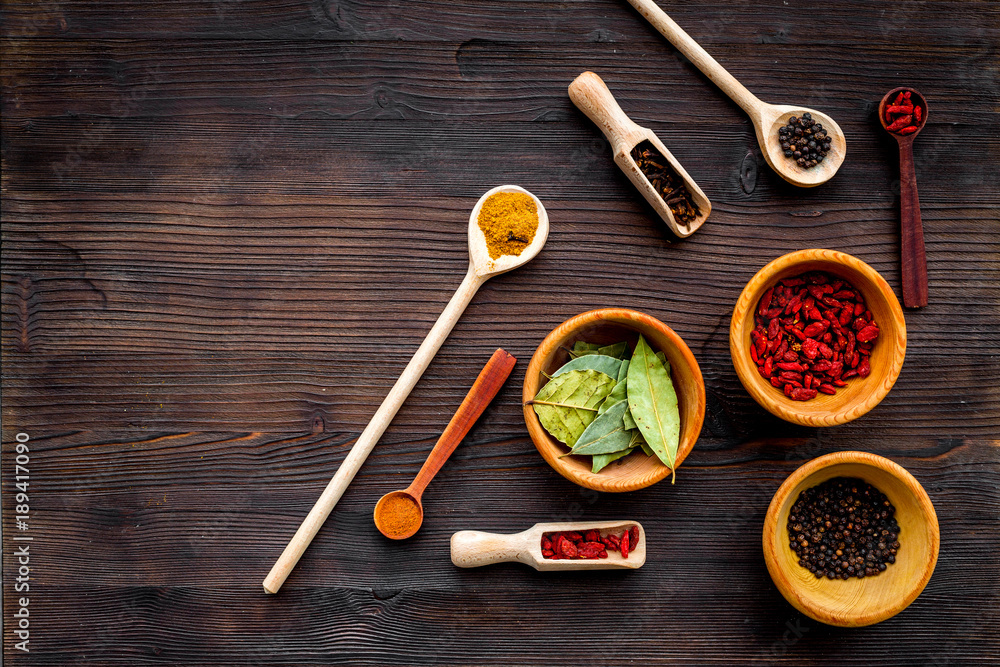 Template for menu design. Empty space near scoops and spoons with spices, bowls with goji, bay leaf, pepper on dark wooden background top view copy space Template for menu design. Empty space near scoops and spoons with spices, bowls with goji, bay leaf, pepper on dark wooden background top view copy space