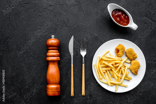 French fries and chicken nuggets with sauces on black background top view copy space