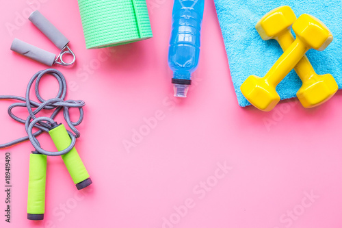Fitness background. Equipment for gym and home. Jump rope, dumbbells, expander, mat, water on pastel pink background top view copy space
