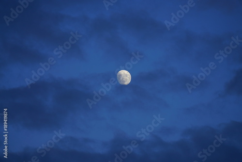 View of the moon in a dark blue sky partially covered by clouds