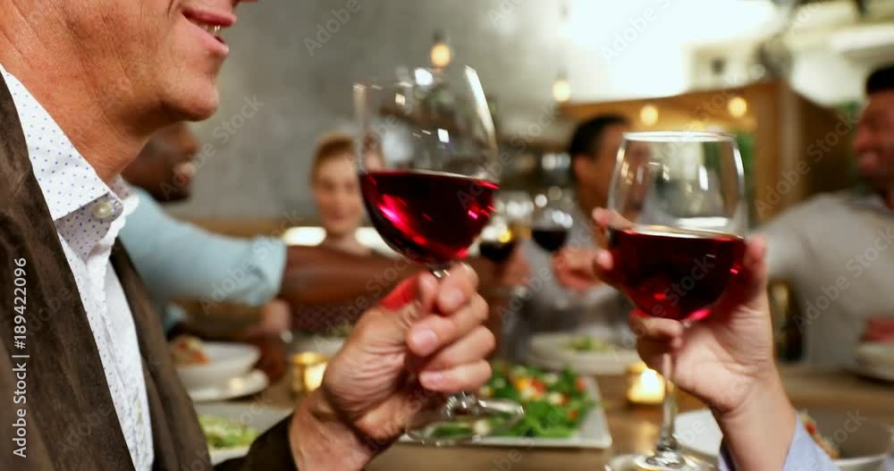 Happy couple toasting wine glasses while friends interacting in background Happy couple toasting wine glasses while friends interacting in background