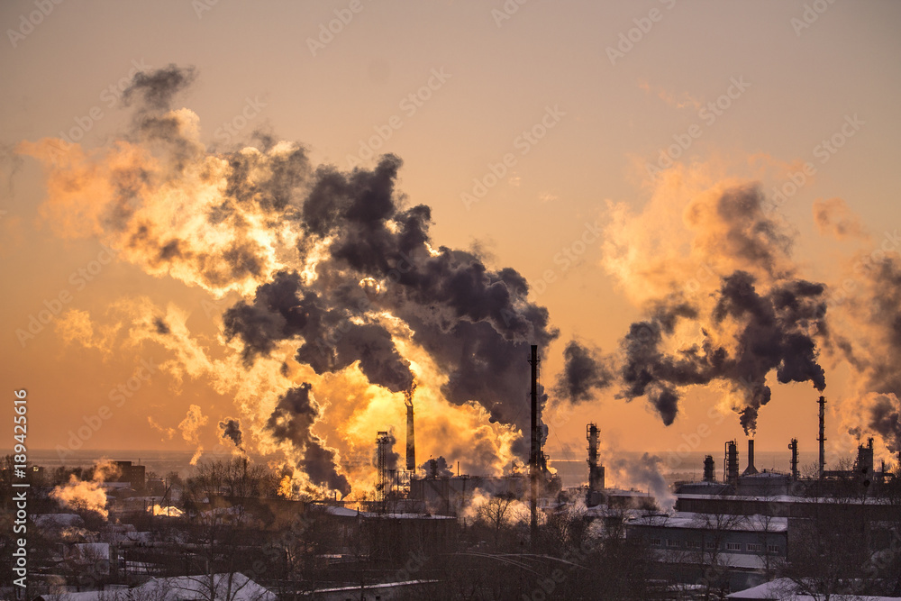 Obraz premium the chimneys of a refinery with smoke and steam with the pinkk sunset on the background
