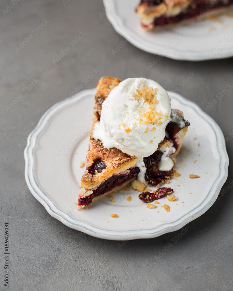 A piece of cherry pie with vanilla ice cream on a white vintage plate on a gray light concrete background. Copy Space. View blank space for text. A piece of cherry pie with vanilla ice cream on a white vintage plate on a gray light concrete background. Copy Space. View blank space for text.