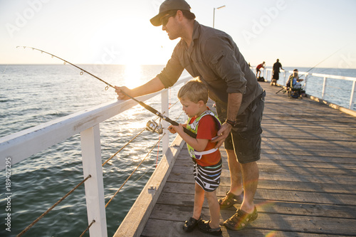 father teaching little young son to be a fisherman, fishing together on sea dock embankment enjoying and learning using the fish rod