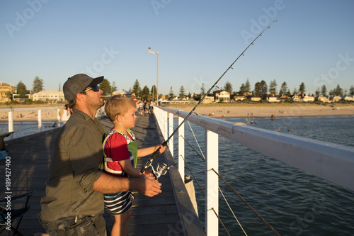 father teaching little young son to be a fisherman, fishing together on sea dock embankment enjoying and learning using the fish rod