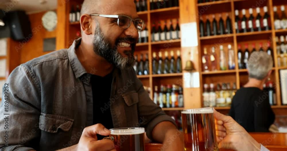 Friends toasting glass of beer at counter in bar Friends toasting glass of beer at counter in bar