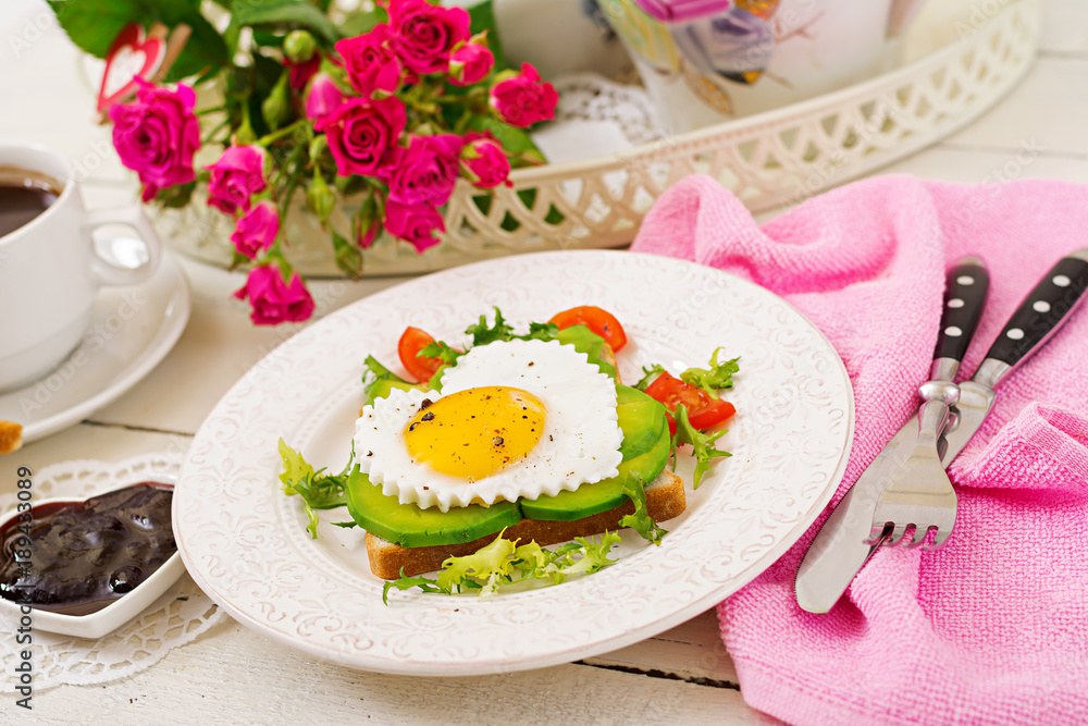 Breakfast on Valentine's Day - sandwich of fried egg in the shape of a heart, avocado and fresh vegetables. Cup of coffee. English breakfast. Breakfast on Valentine's Day - sandwich of fried egg in the shape of a heart, avocado and fresh vegetables. Cup of coffee. English breakfast.