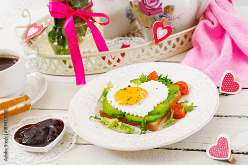 Breakfast on Valentine's Day - sandwich of fried egg in the shape of a heart, avocado and fresh vegetables. Cup of coffee. English breakfast.