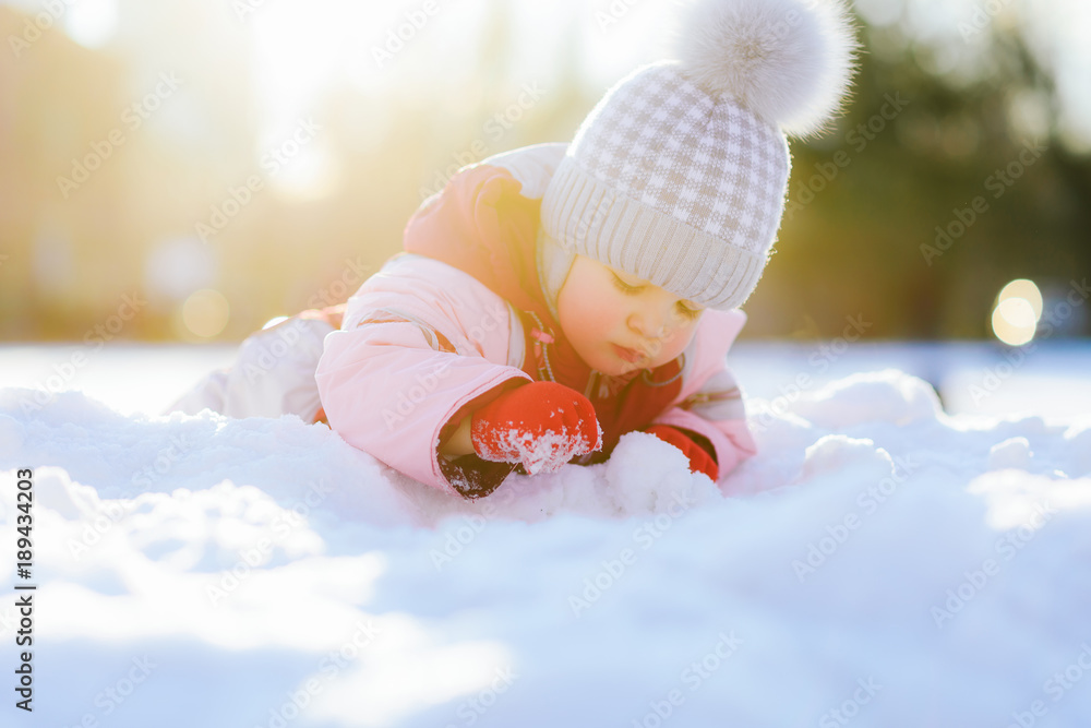 small child crawls on snow against the background of a sunset in winter - obrazy, fototapety, plakaty 
