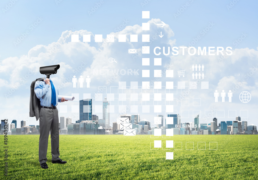 Camera headed man standing on green grass against modern cityscape