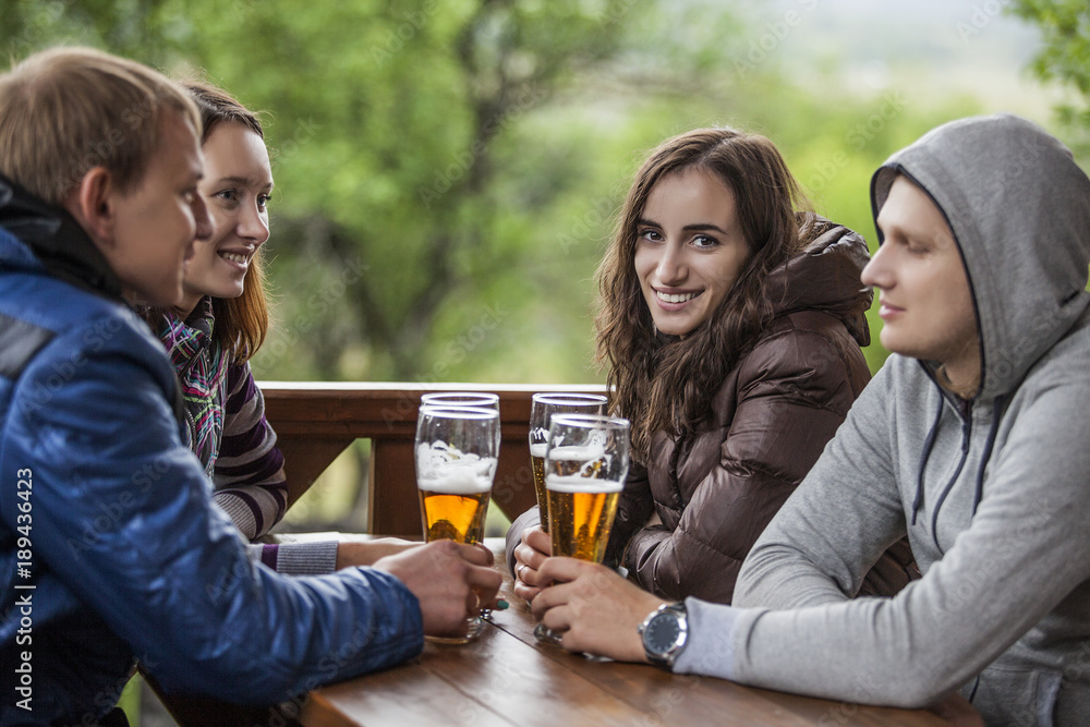Happy friends sitting with tall glasses of beer in hand at a wooden table Happy friends sitting with tall glasses of beer in hand at a wooden table