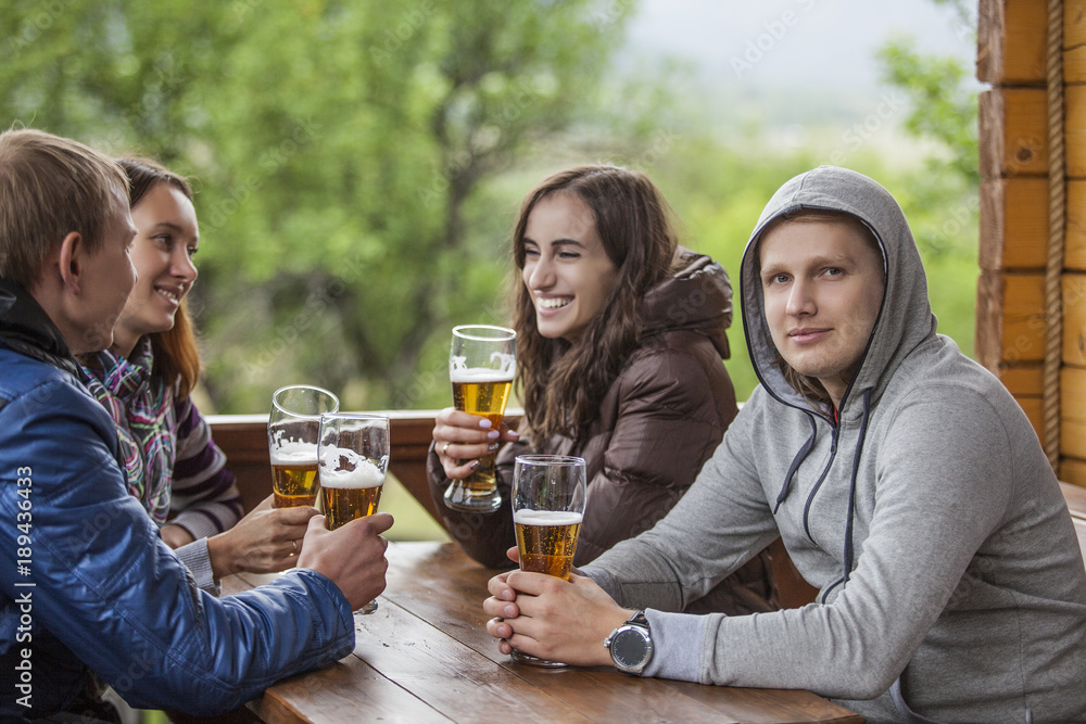 Happy friends sitting with tall glasses of beer in hand at a wooden table Happy friends sitting with tall glasses of beer in hand at a wooden table
