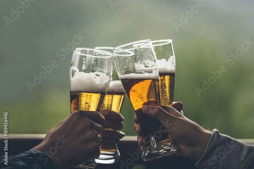 Fototapeta Beer with foam light tall boys in the hands of friends raising a toast closeup