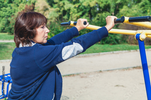 elderly woman performs exercises on simulators on summer sports ground