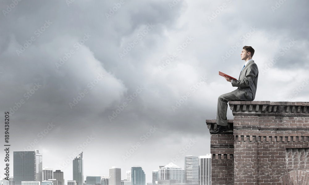 Man on roof edge reading book and cityscape at background Man on roof edge reading book and cityscape at background