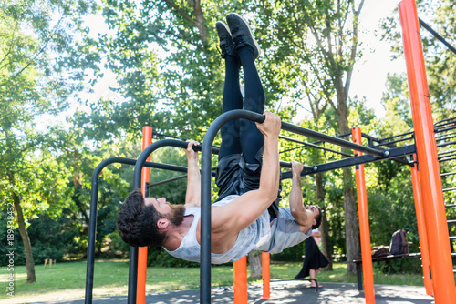 Two muscular young men practicing together calisthenics workout for strength and balance in an outdoor fitness park with modern equipment