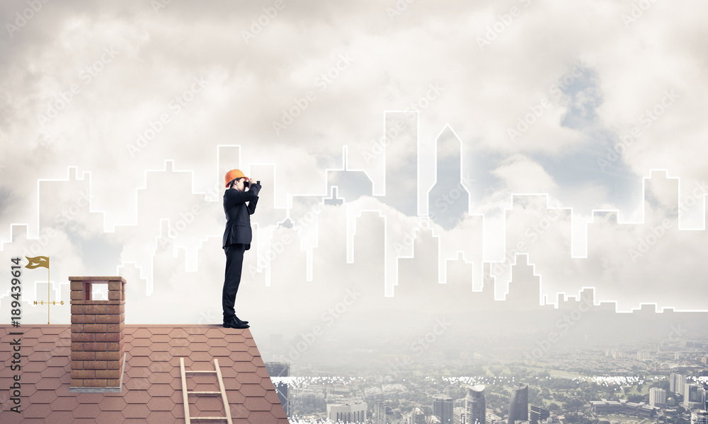 Engineer man standing on roof and looking in binoculars. Mixed m Engineer man standing on roof and looking in binoculars. Mixed m