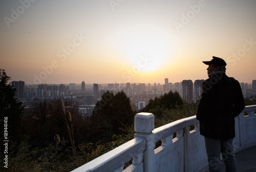 Over the city, a man stands on the top of the mountain to see the city