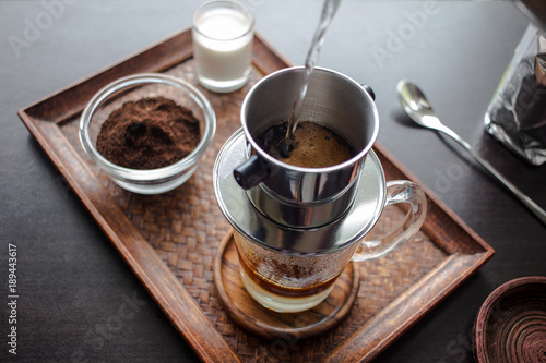 Картината върху платно Drip, Brewing, pouring water over ground coffee contained in Vietnamese Phin Filter on dark wooden board