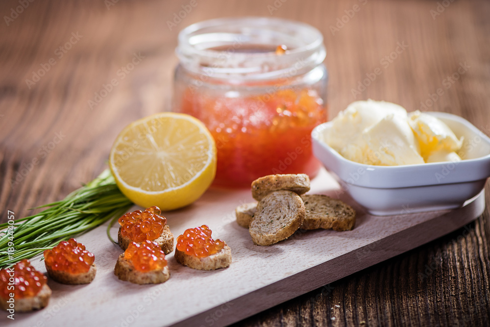 side view od tasty fresh salmon roe red caviar with butter and baquette on wood table side view od tasty fresh salmon roe red caviar with butter and baquette on wood table