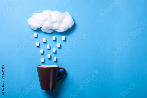 From the cloud it rains or snow in the form of cubes of sugar in a cup. Blue background. Copy space for text