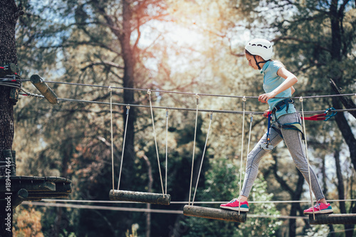 Happy school girl enjoying activity in a climbing adventure park on a sunny day