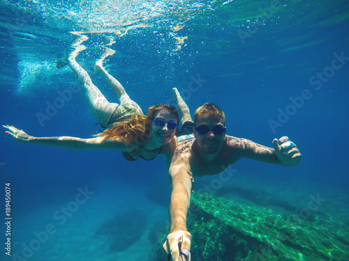 Underwater selfie with a stick of a young attractive love couple swimming in the turquoise sea under the surface for summer vacation.