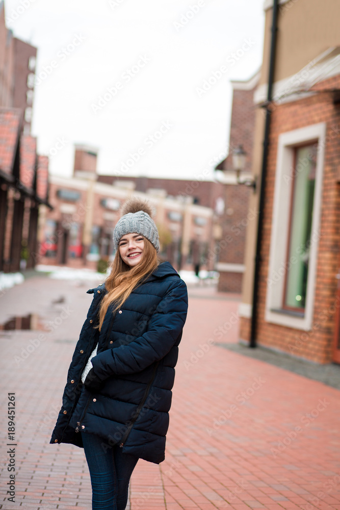 Fototapeta premium Happy young woman wearing black winter coat and knitted hat posing at the street in Kiev