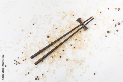 top view of raw rice and spices spilled on white surface with chopsticks