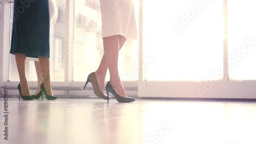 Girls in dresses walk on long heels along the window on the floor with glare. HD, 1920x1080, slow motion