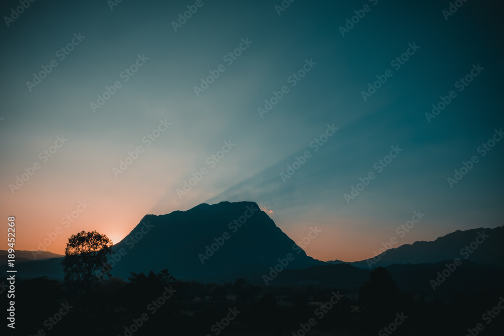 The sunset and sunlight behind a big mountain with clear sky in the evening