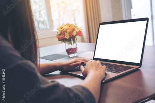 Mockup image of woman's hands using and typing on laptop with blank white desktop screen on wooden table in the house © Farknot Architect