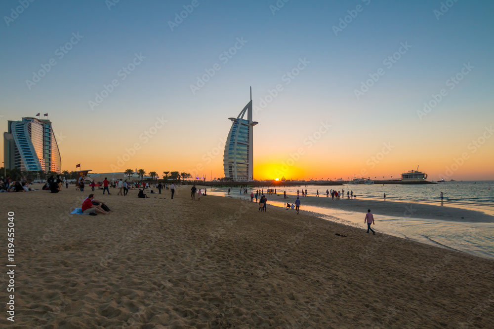 Naklejka premium People waiting for new year celebration at the beach in last day of the year. The world's first seven stars luxury hotel Burj Al Arab and Dubai Marina in background 
