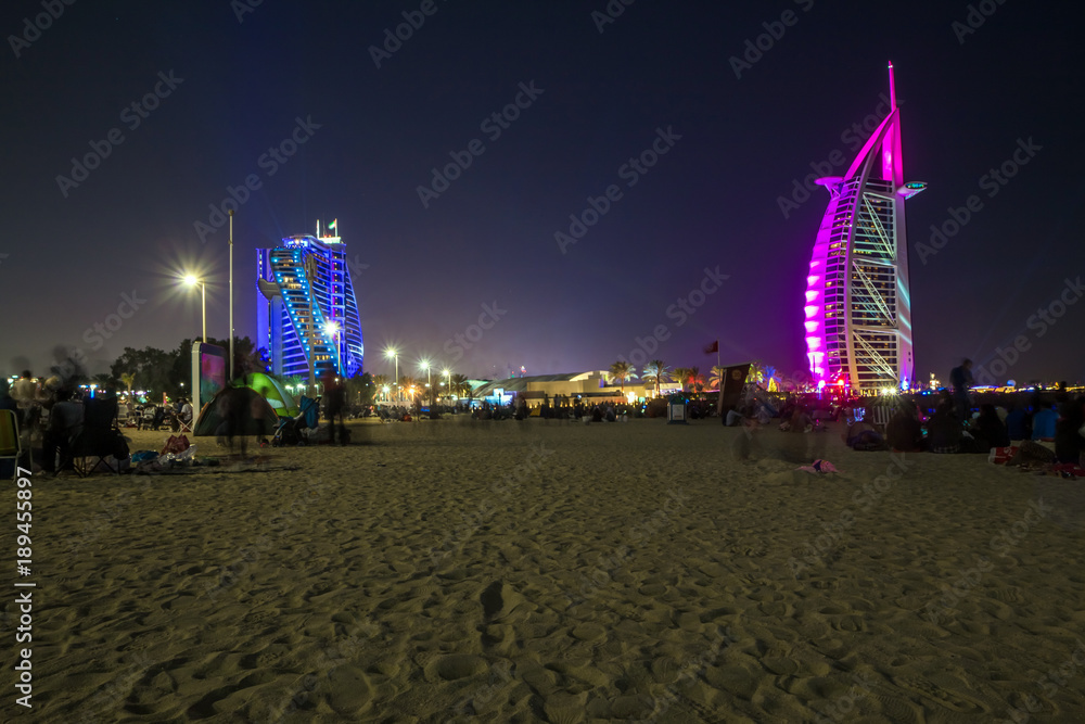 Naklejka premium People waiting for new year celebration at the beach in last day of the year. The world's first seven stars luxury hotel Burj Al Arab and Dubai Marina in background 