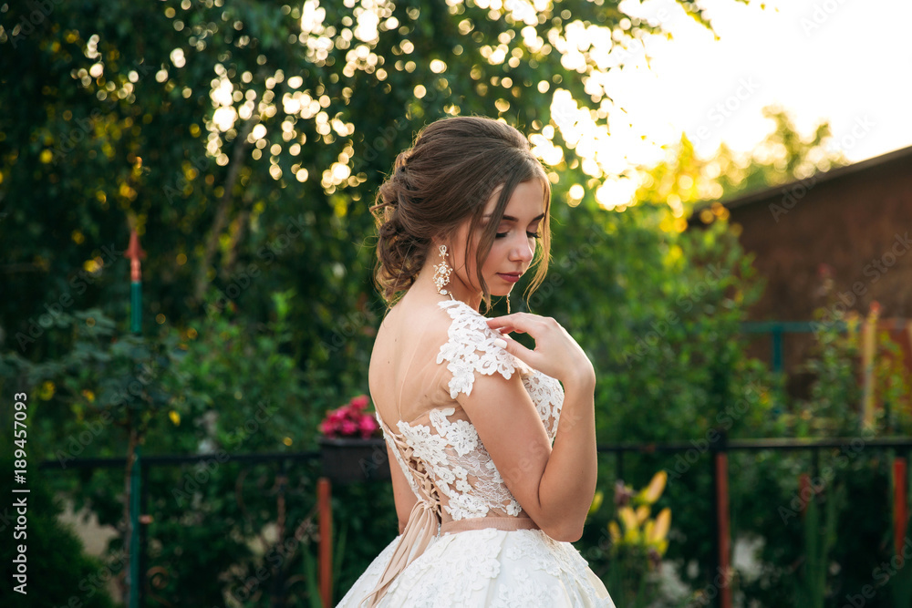 Young girl in wedding dress in park posing for photographer. Sunny weather, summer