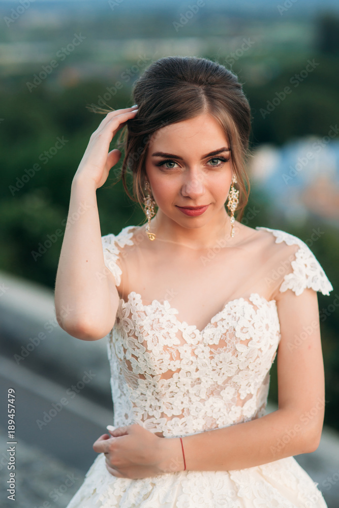 Naklejka premium Young girl in wedding dress on city background at sunset. Summer