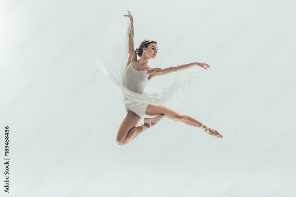 young elegant ballerina in white dress jumping in studio, isolated on white