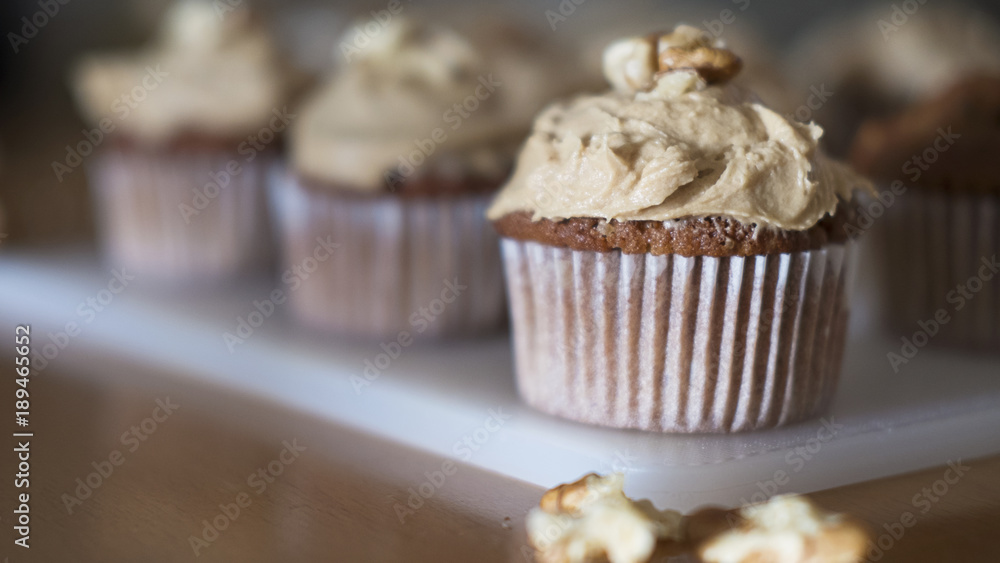 Horizontal shot of coffee and walnuts homemade cupcakes with coffee icing, just taken out of the oven, positioned on a rustic white plastic board, indulgent dessert with considerable amount of sugar Horizontal shot of coffee and walnuts homemade cupcakes with coffee icing, just taken out of the oven, positioned on a rustic white plastic board, indulgent dessert with considerable amount of sugar