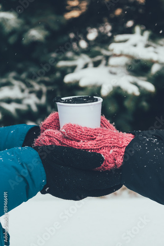 partial view of couple holding thermocup with hot drink together in winter forest photo