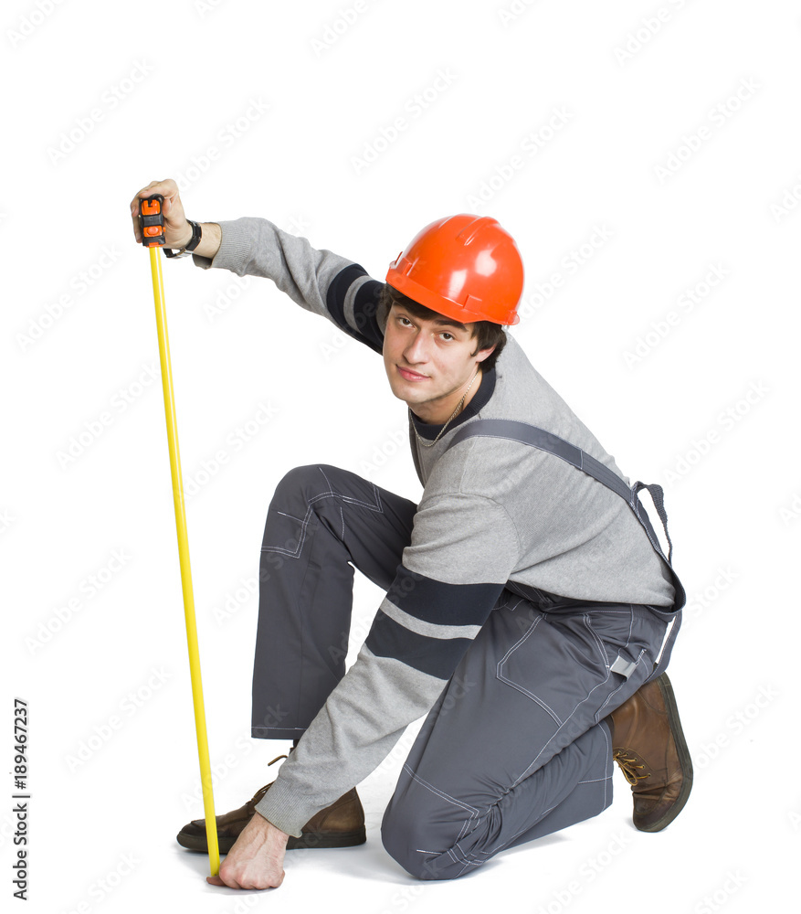 A young man in working grey clothes and orange hard helmet measuring the metric area in the room. A young man in working grey clothes and orange hard helmet measuring the metric area in the room.