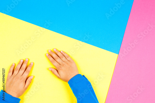 Kid hands on yellow, blue and pink background.