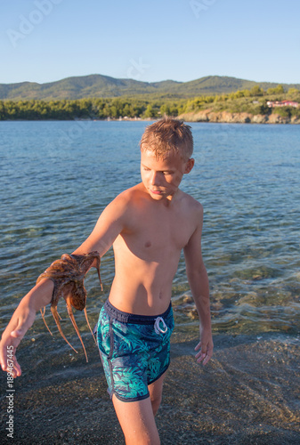 A cute teenager with octopus on his hand bakground of the sea photo