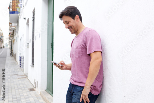 middle aged man standing outside and reading text message on his mobile phone