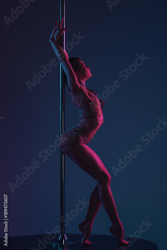 side view of seductive young female dancer leaning at pole on blue
