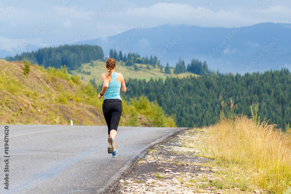 Young sporty woman jogging on mountain road. Running fitness girl in sportswear outdoor image with copy space