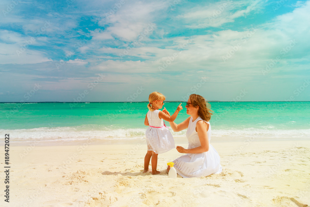 mother and daughter applying sunblock cream on beach