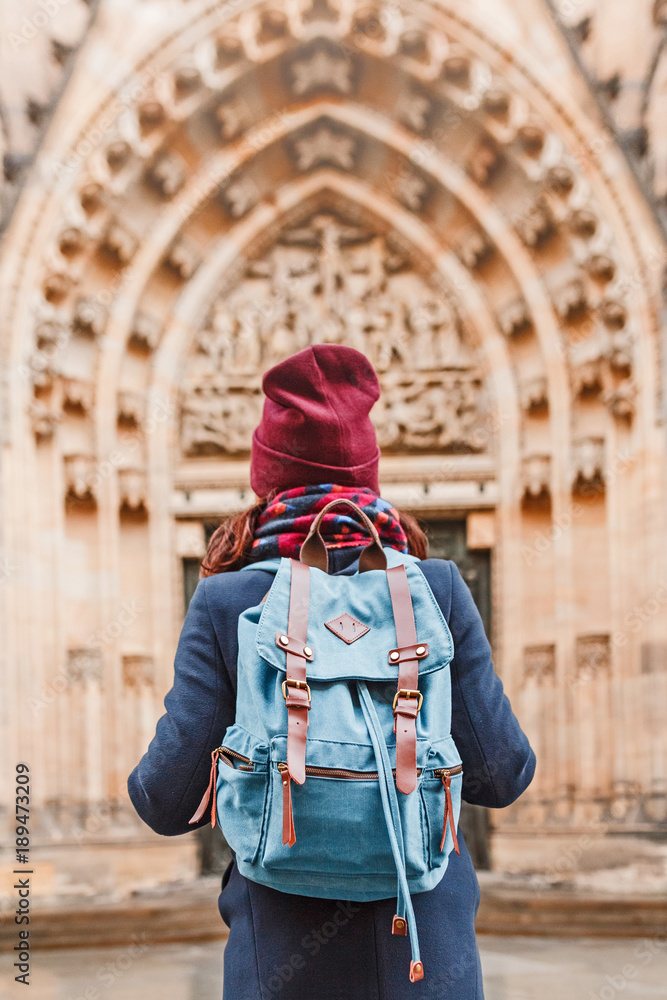 Fototapeta premium rear view of a traveler woman with backpack looking at historical architecture, sightseeing tour concept